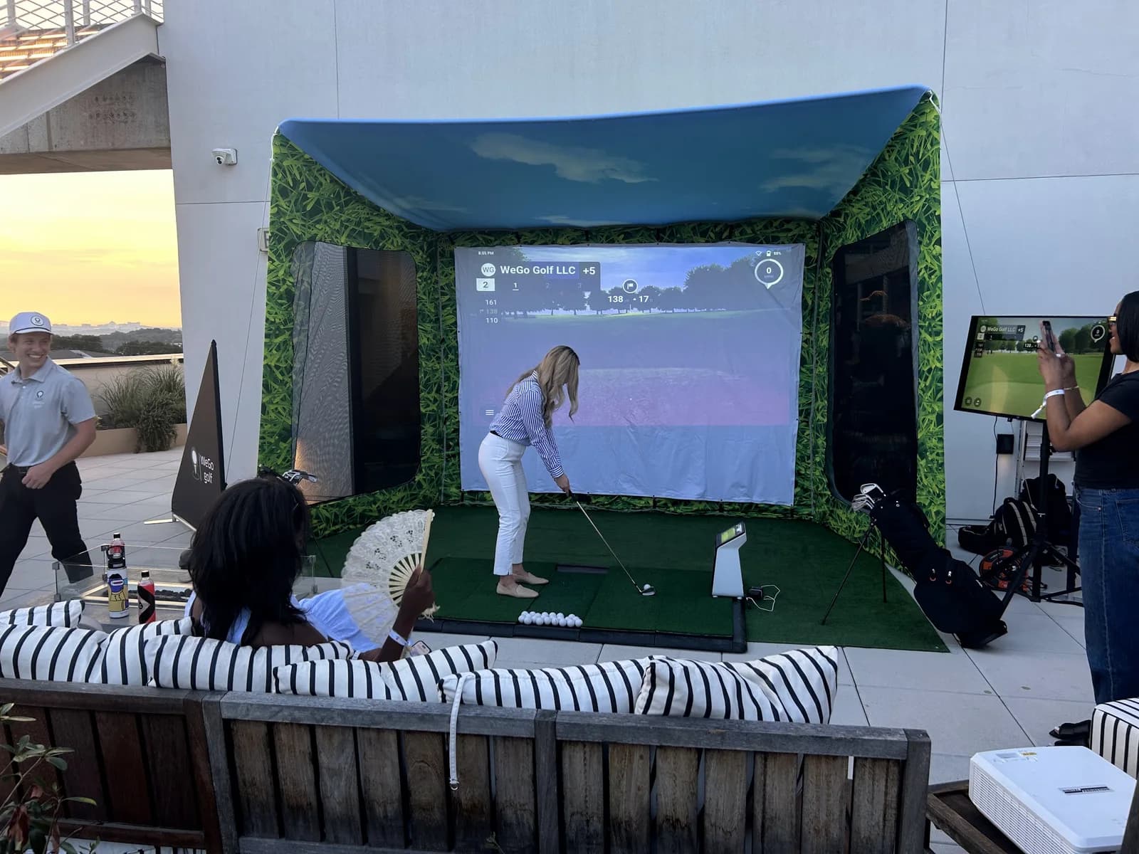 Guest teeing off in a WeGo Golf bay on a rooftop terrace at sunset