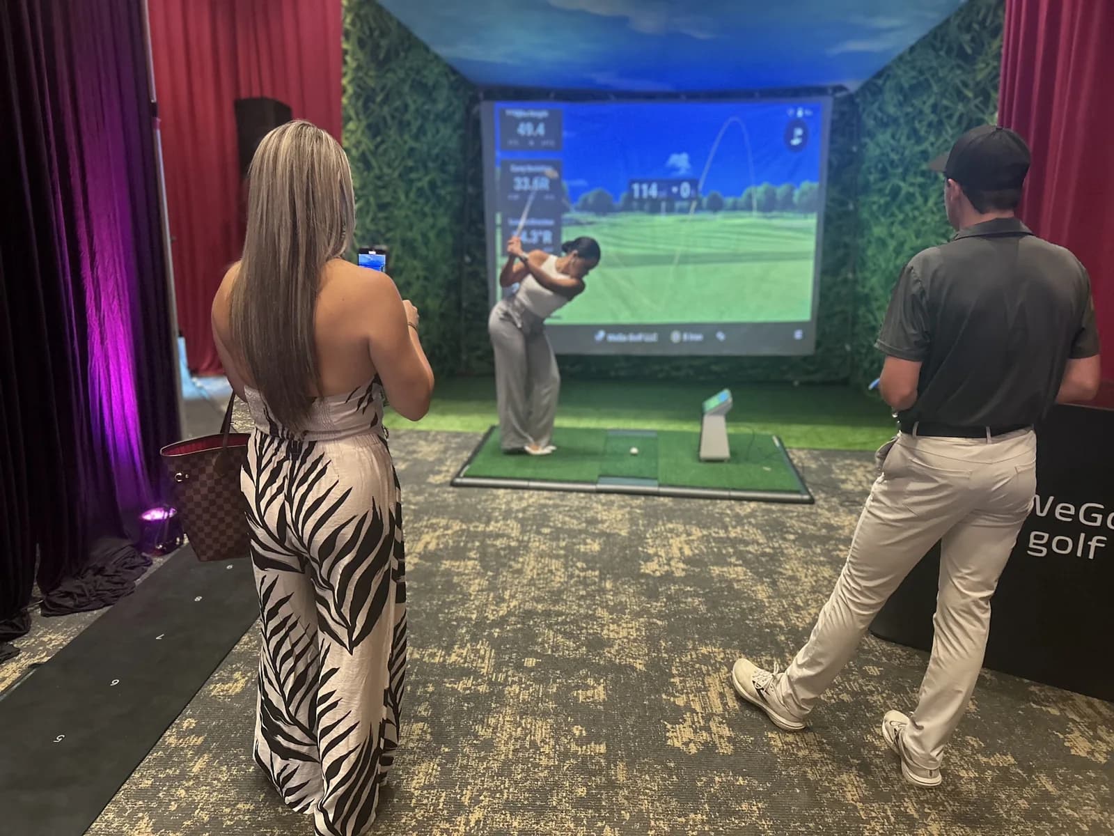Spectators watching a guest play a WeGo Golf simulator at an evening event