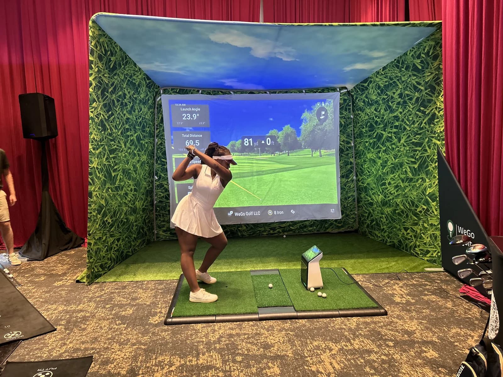 Guest mid-swing in a WeGo Golf hitting bay at Urban Golf Week, live launch data on screen